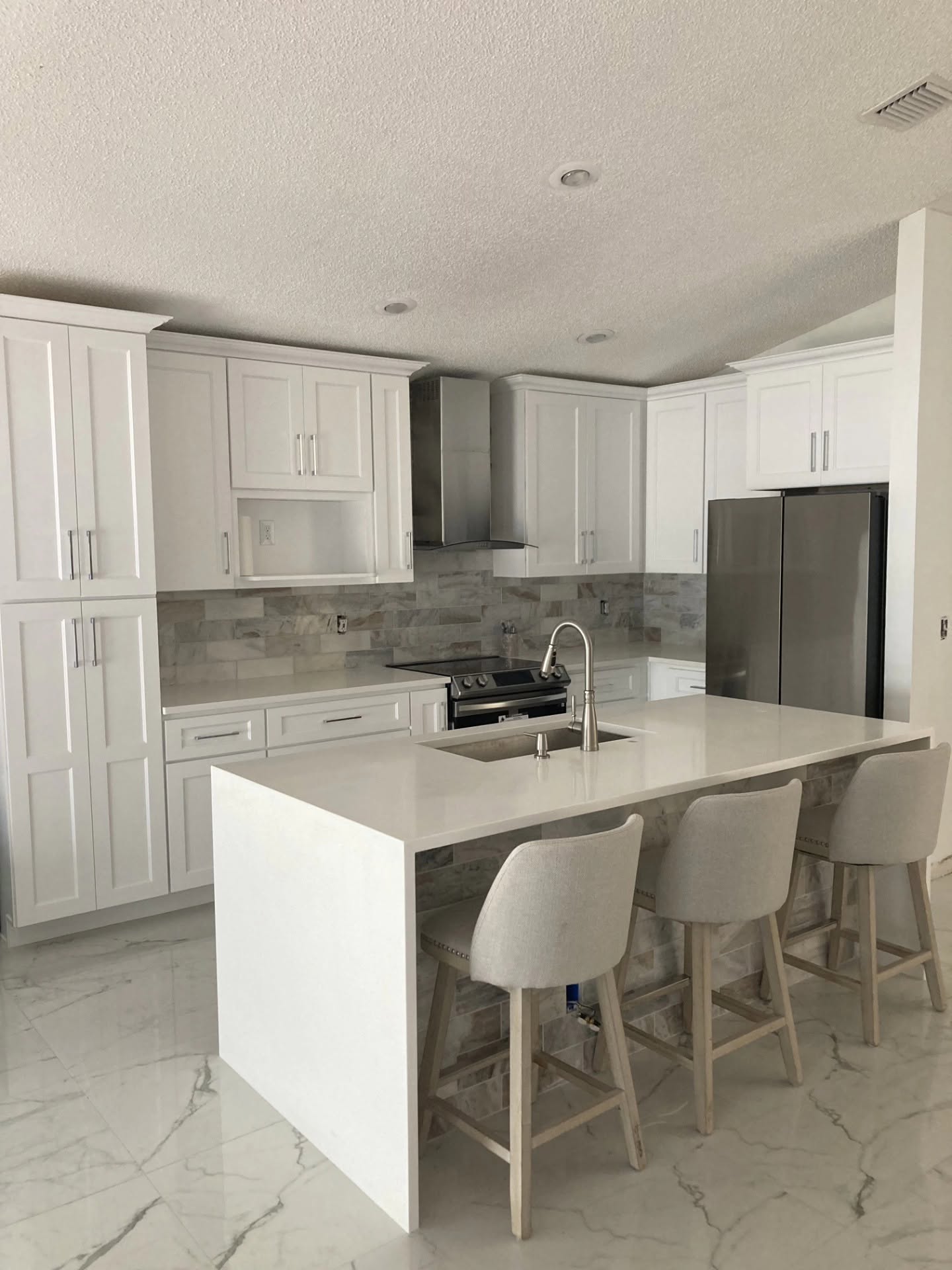 Kitchen remodel with white cabinets, tile backsplash, and center island